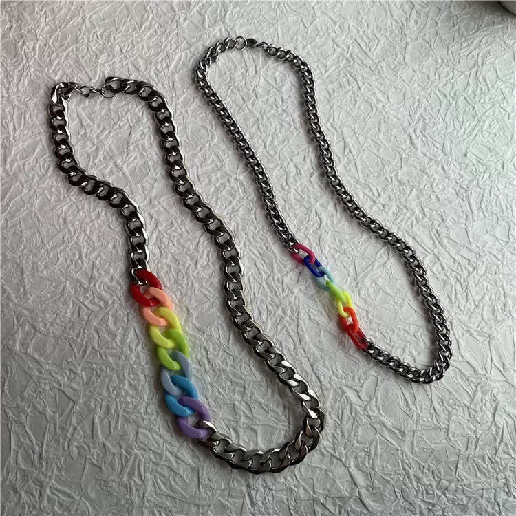 A silver-toned chain necklace with two colorful links: one featuring a rainbow gradient from red to purple, and the other featuring a red, yellow, green, and blue gradient. The necklace is displayed on a textured white surface.