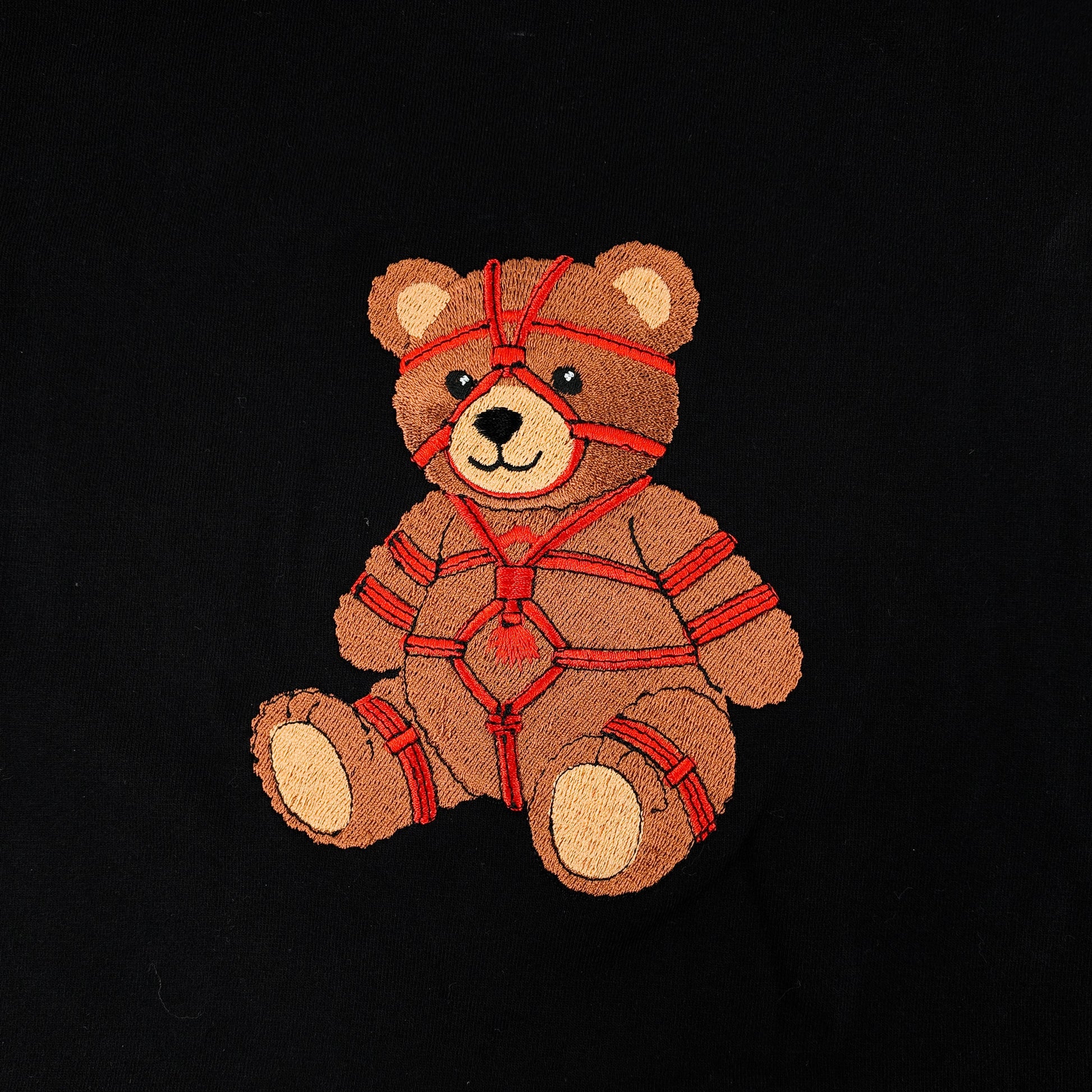 Black t-shirt with embroidered teddy bear graphic wrapped in red rope detailing